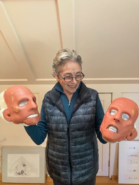 Judith, an older woman, holding two Odo masks